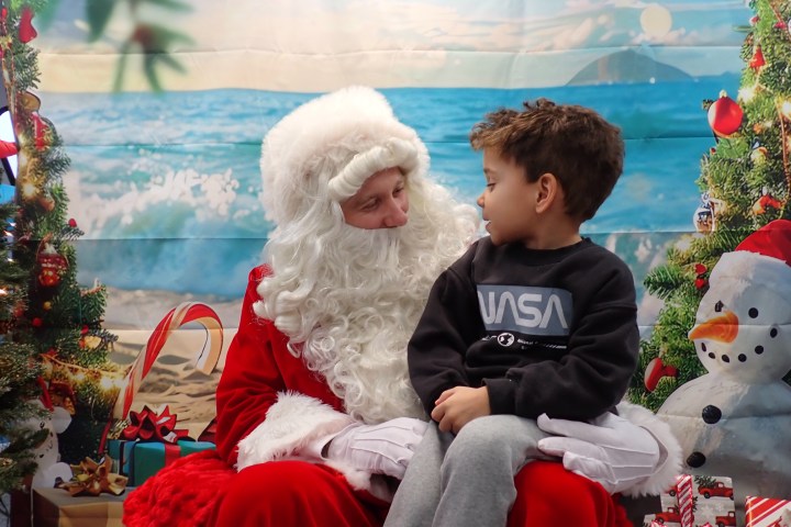 Child sitting on Santa's lap with beach backdrop.