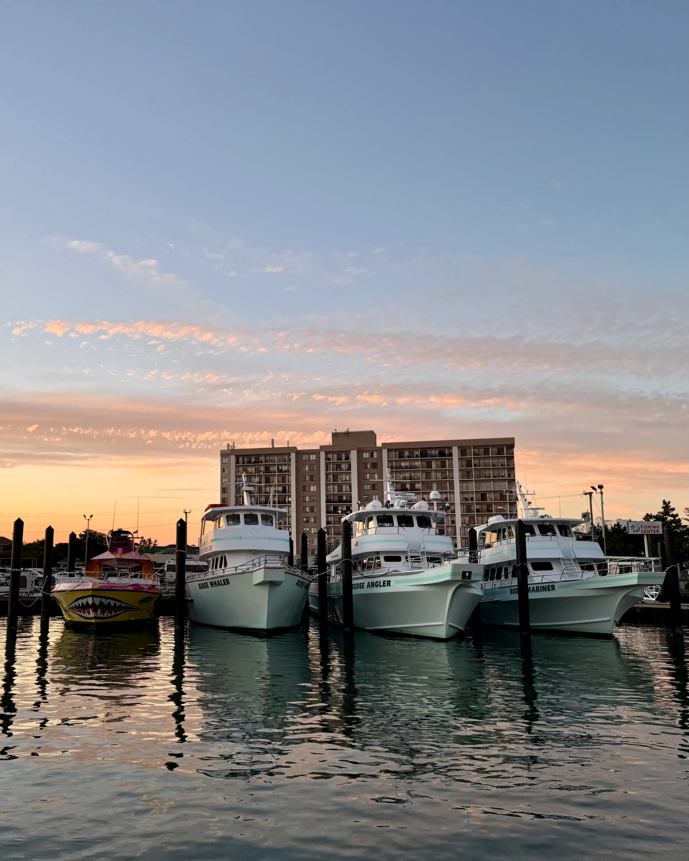 Boats docked at sunset with a building in the background and colorful sky.