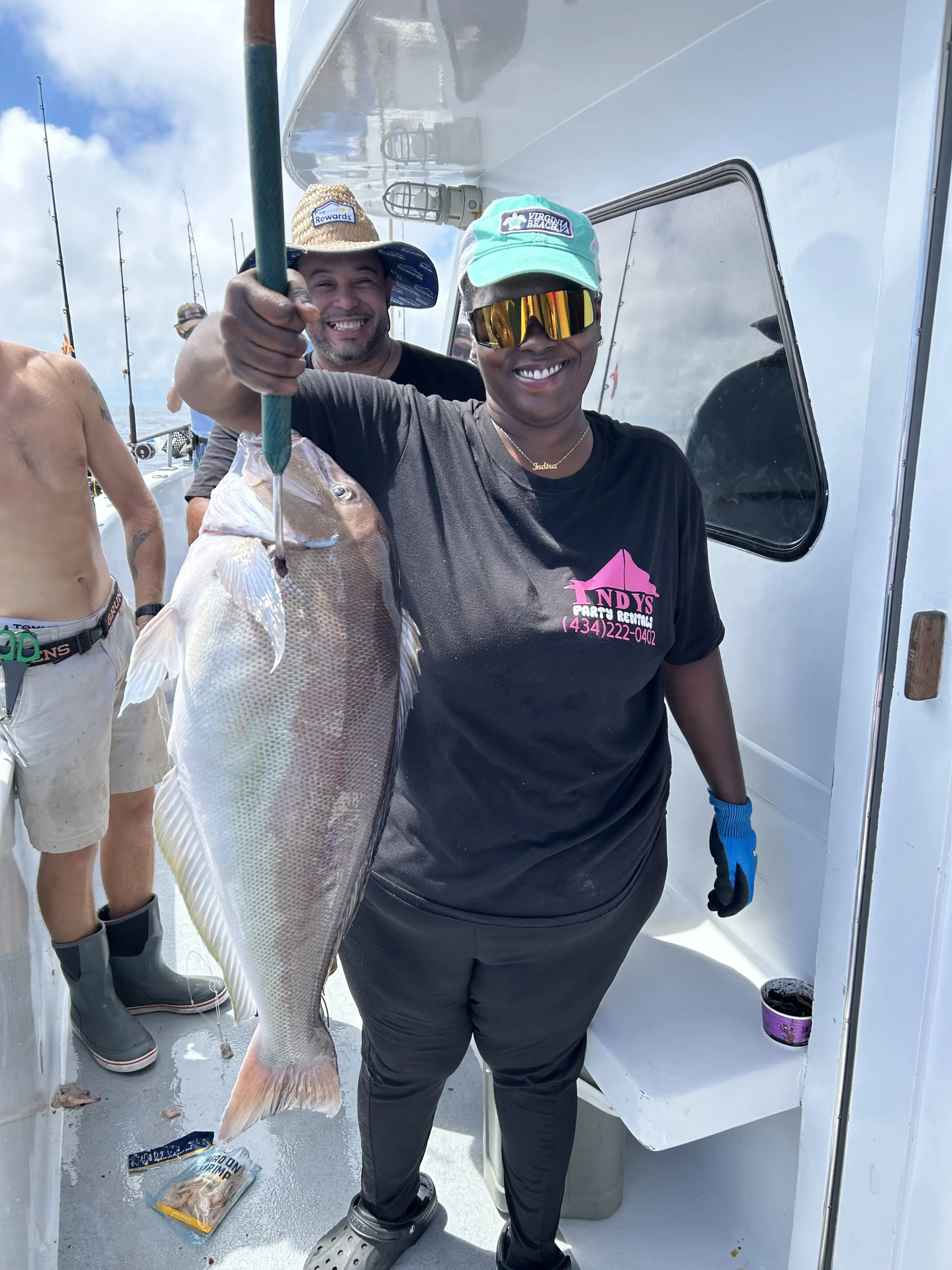 Smiling person on a boat holding a large fish with others in the background.
