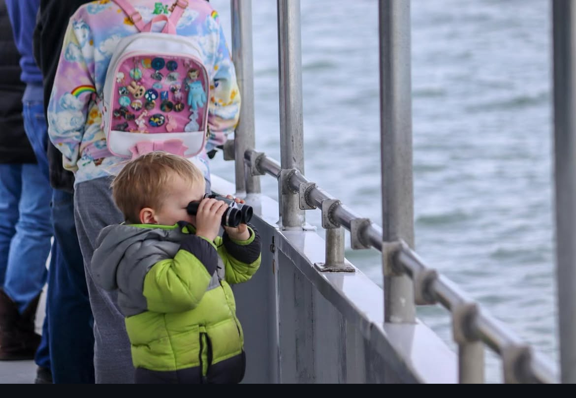 Child using binoculars on a boat, looking for wildlife.