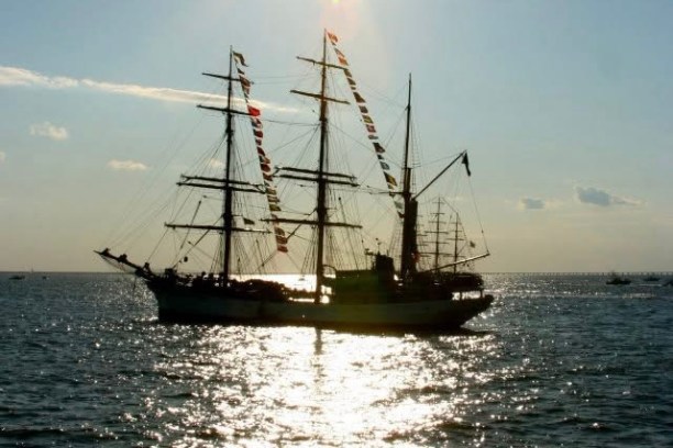 Silhouette of a tall ship with sails on a sunny sea.