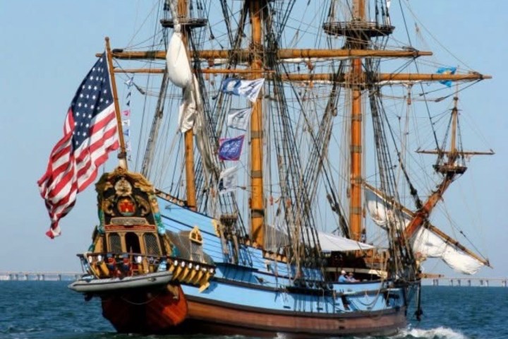 Colorful tall ship with U.S. flag sails on water under clear sky.