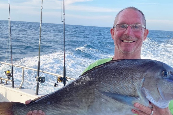 Man on boat holding large fish, with fishing rods in the background.