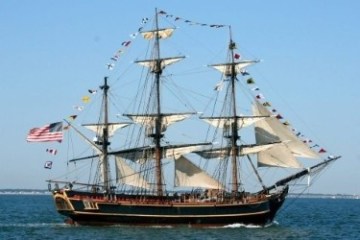 Large sailing ship with tall masts and flags, moving on water.