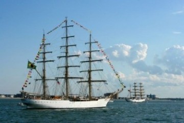 Two tall ships with sails and flags on ocean with blue sky.