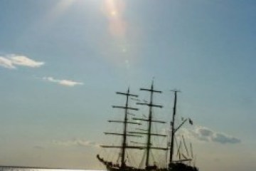 Silhouette of a tall ship sailing on the ocean under a bright sun.