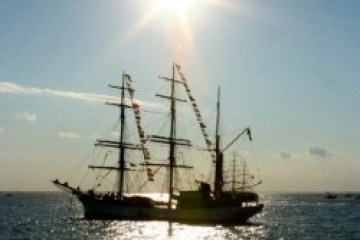 Sailing ship silhouetted against sunlit sea under a bright sun.