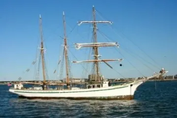 A three-masted sailing ship on the water under a clear blue sky.
